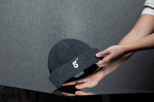 Short:  Hands holding a Schvitzin merino wool felt sauna hat  Medium (recommended):  Two hands cradling a charcoal gray Schvitzin merino wool felt sauna hat with embroidered "S" logo against a dark gray background