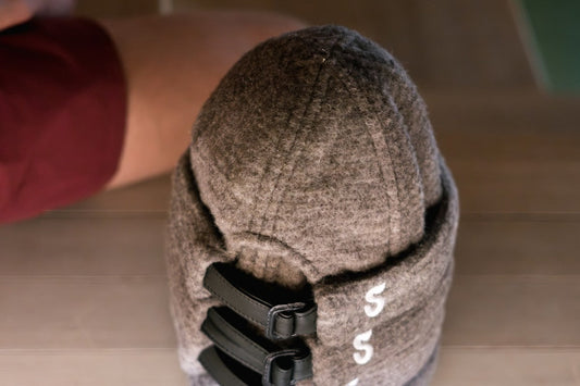 Overhead view of a charcoal gray Schvitzin wool felt sauna hat with black leather adjustable buckle straps and embroidered "S" logo