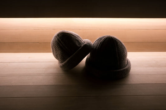 Two merino wool sauna hats resting on a wooden sauna bench, warm ambient backlight