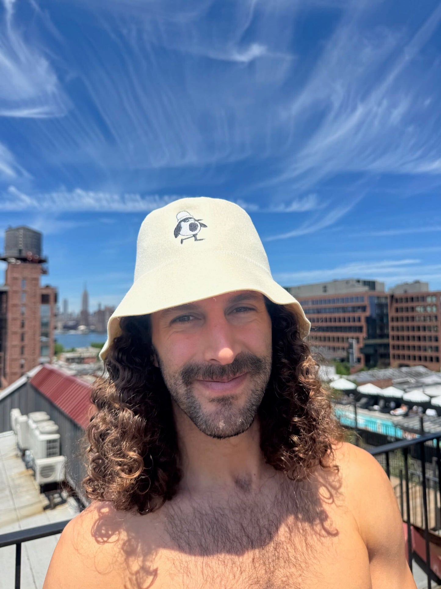 Person wearing the Natural Cream colorway Schvitzin Starter merino wool sauna hat on a Brooklyn rooftop with the NYC skyline in the background