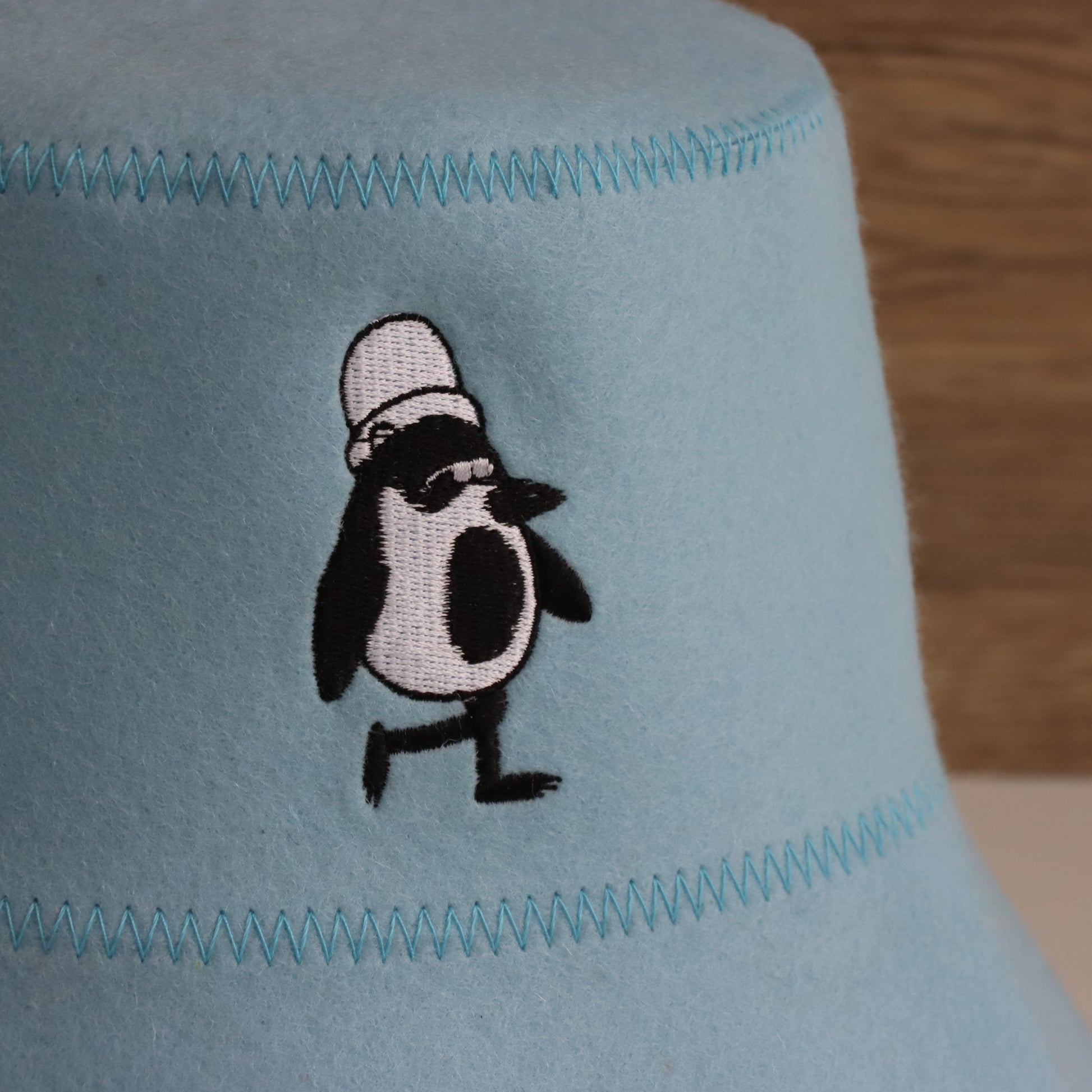 Close-up of Vanya the Penguin embroidery on the Sky colorway Schvitzin Starter merino wool sauna hat