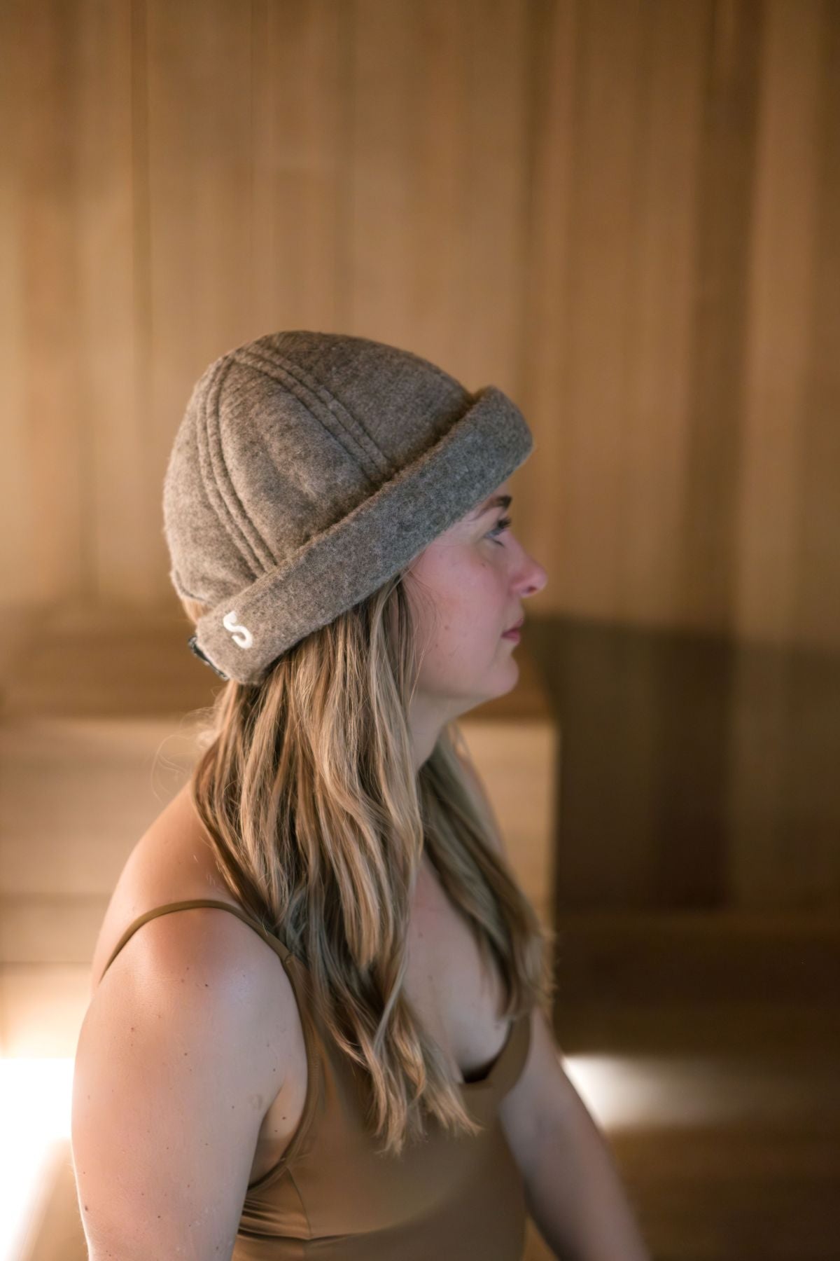 Woman wearing heather gray wool sauna hat with rolled brim in sauna setting