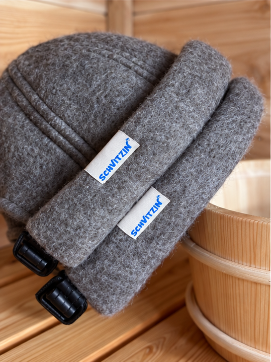 Two grey Schvitzin merino wool sauna hats with woven labels on a sauna bench